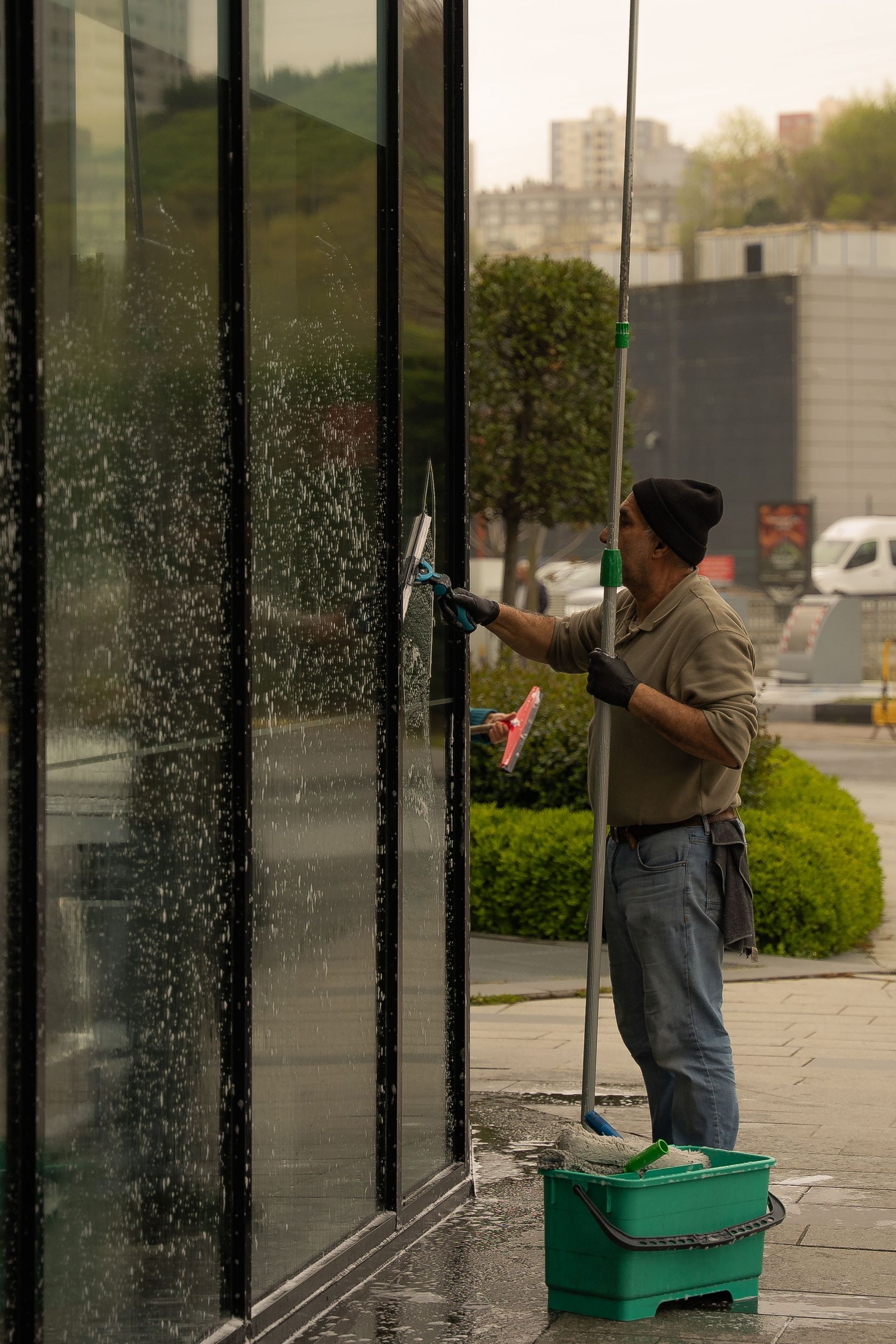 A window cleaner using a squeegee to clean a glass building facade on a cloudy day.